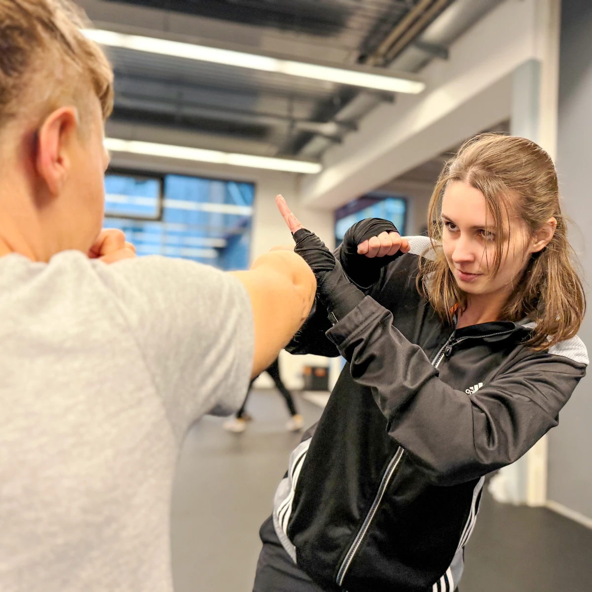 Zwei Frauen im Gruppentraining für Erwachsene: Eine Frau demonstriert die Abwehr gegen einen geraden Punch.